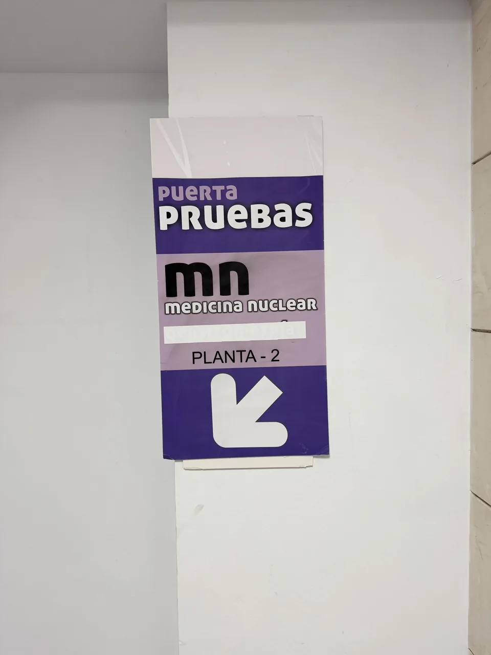 Cartel violeta Puerta Pruebas, MN Medicina Nuclear, planta −2, con flecha diagonal hacia abajo a la izquierda.